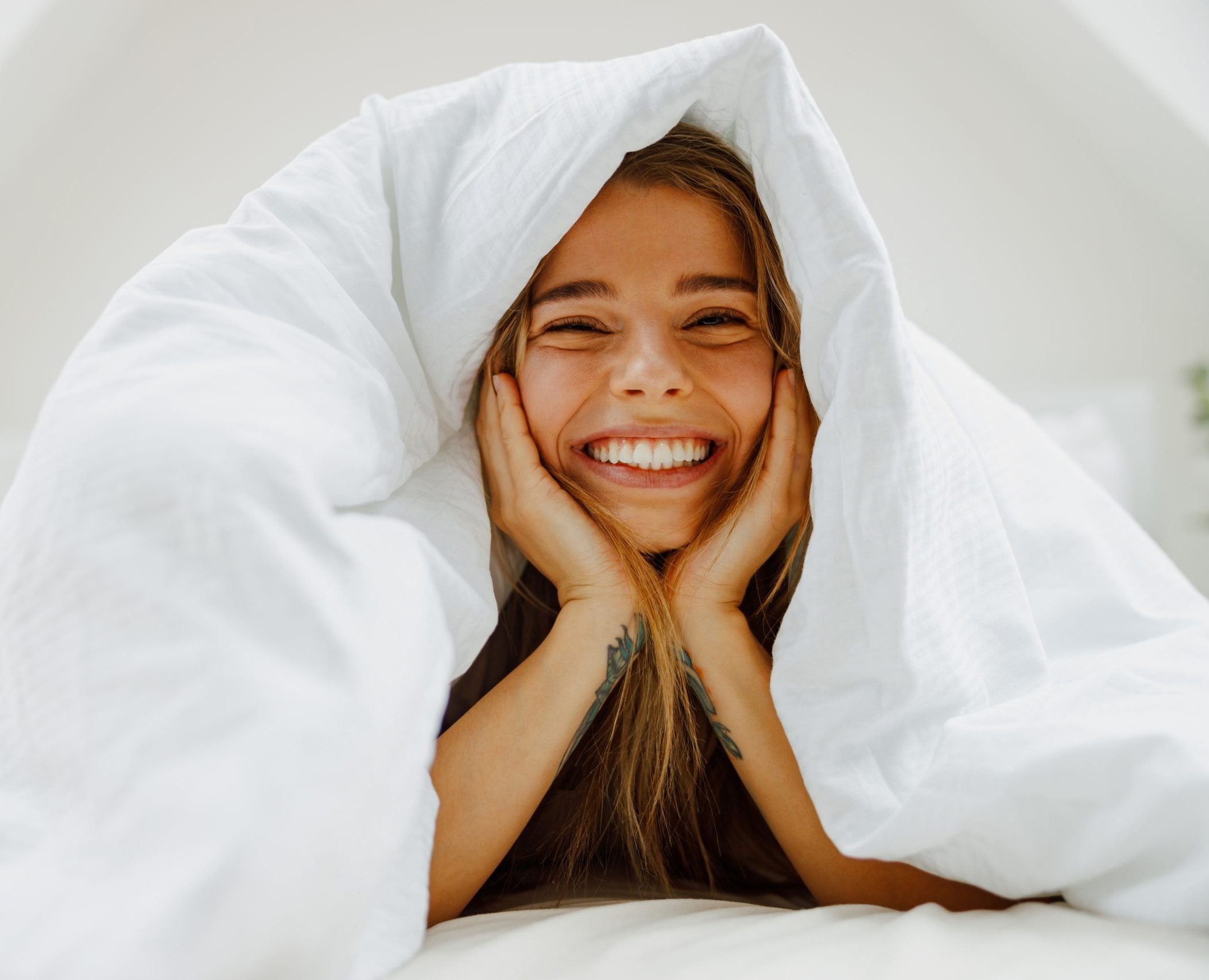A,Woman,Lays,In,Bed,Under,A,White,Blanket,,Smiling